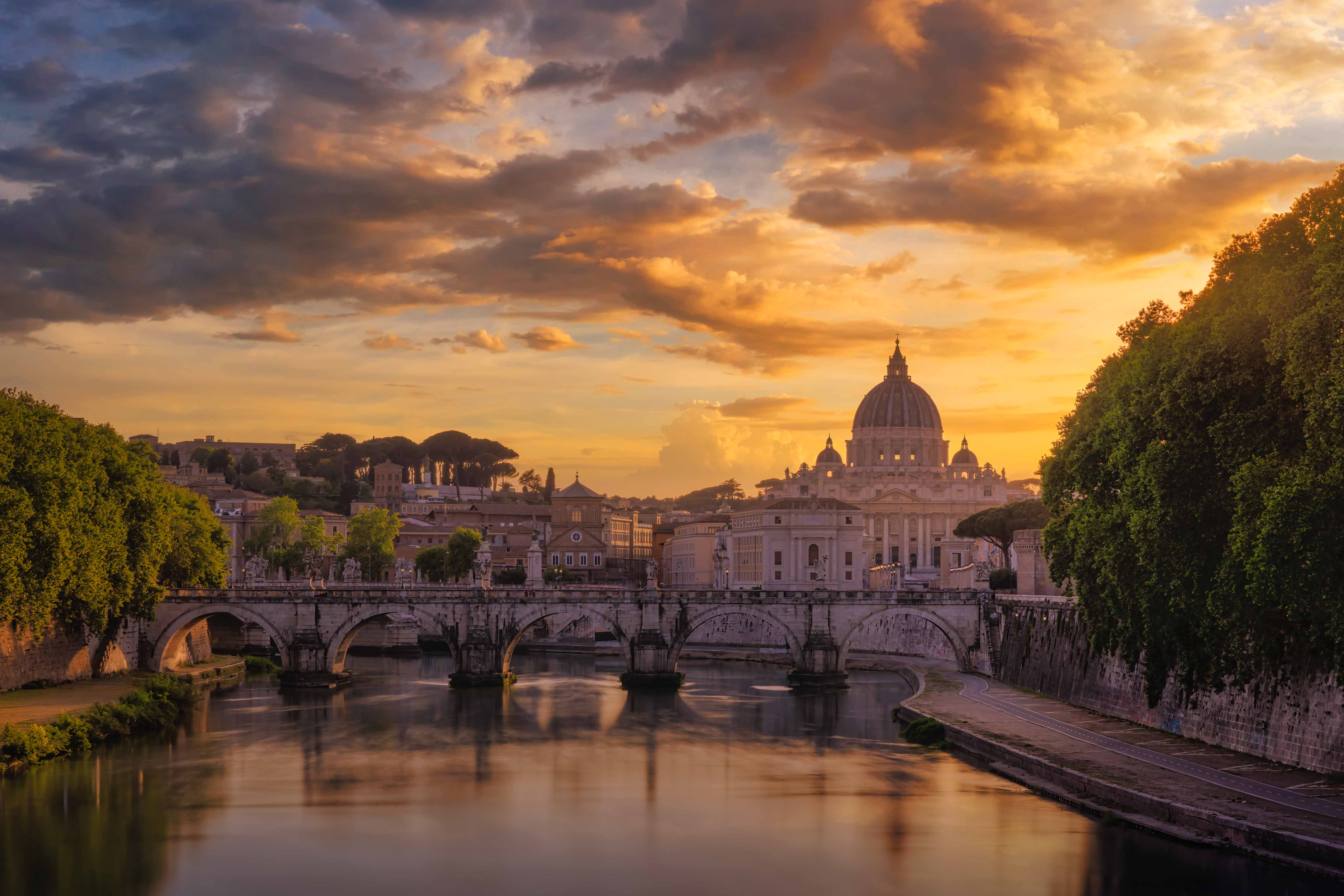 St. Peter's Basilica and the Vatican seen across the Tiber at dusk, Michelangelo's dome rising above Roman rooftops in warm evening light