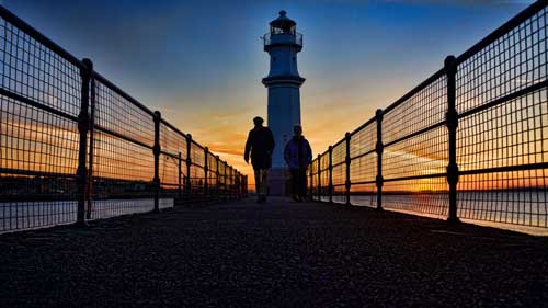 Fine art silhouette photograph of a couple walking back from the vista of New Haven Lighthouse in Scotland.